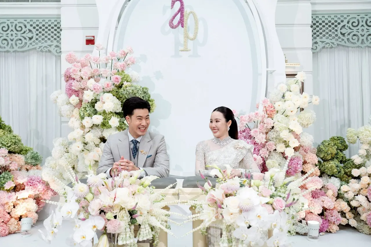 บ่าวสาวยิ้มที่โต๊ะพิธี ล้อมรอบด้วยกล้วยไม้ขาวและชมพู